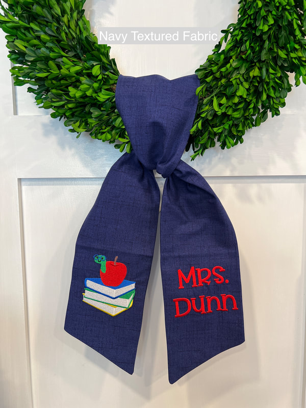 Teacher wreath sash with bookworm, stack of books and embroidered personalized name.